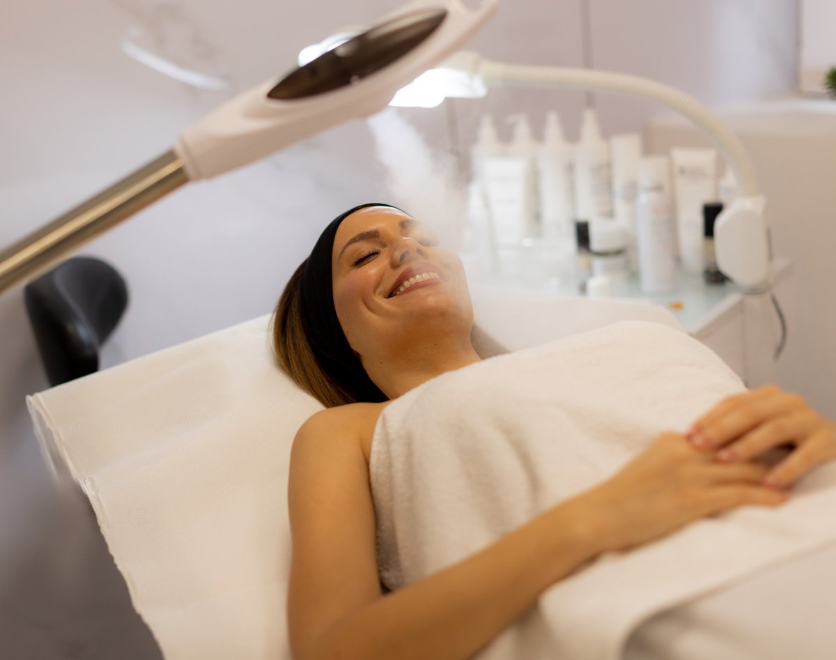 A tranquil spa setting features a woman enjoying a facial treatment, with mist enveloping her face.